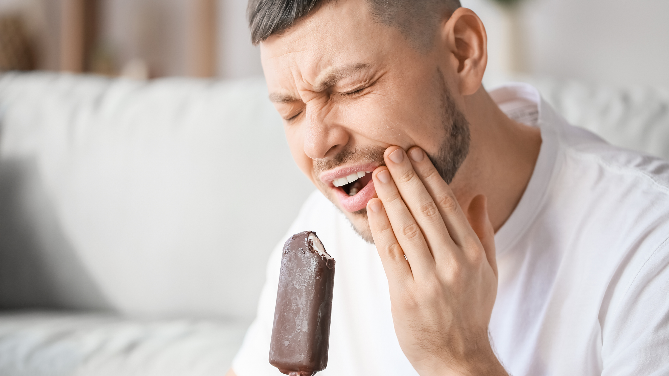 Hombre joven sufre sensibilidad dental al comer un helado