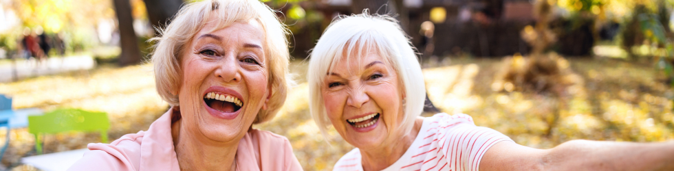 Dos mujeres mayores sonriendo con confianza en un parque tras recuperar sus dientes fijos en 24 horas