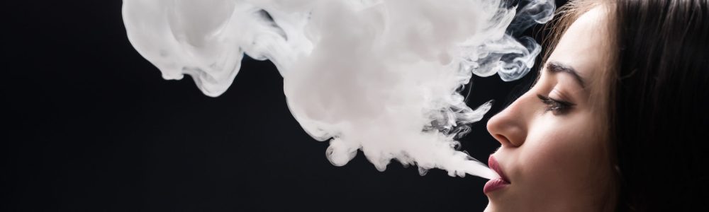 Beautiful woman is vaping. Dark background. Studio shooting.