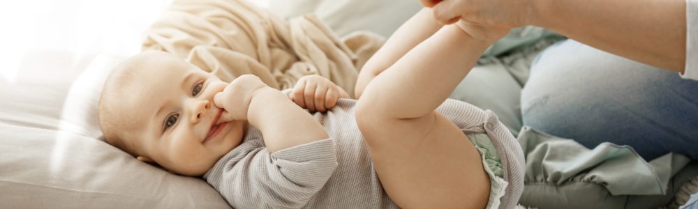 Close up portrait of little newborn son looking at camera while playing with mother. Kid smiling and put his fingers in mouth lookin happy and carefree