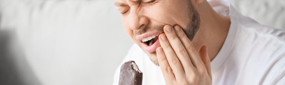 Hombre joven sufre sensibilidad dental al comer un helado